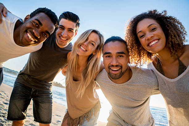 Happy group of friends at the beach hugging in a circle and looking at the camera smiling