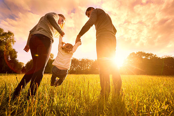 Happy family in the park evening light. The lights of a sun. Mom, dad and baby happy walk at sunset. The concept of a happy family.Parents hold the baby's hands.